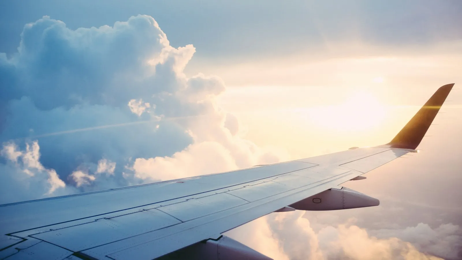 An airplane wing over clouds with a distant coastline below